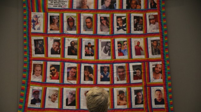 A woman stares at a quilt with the faces of the 49 victims of the Pulse shooting.