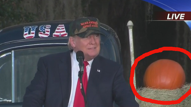 An usually orange Trump sits behind podium on hay