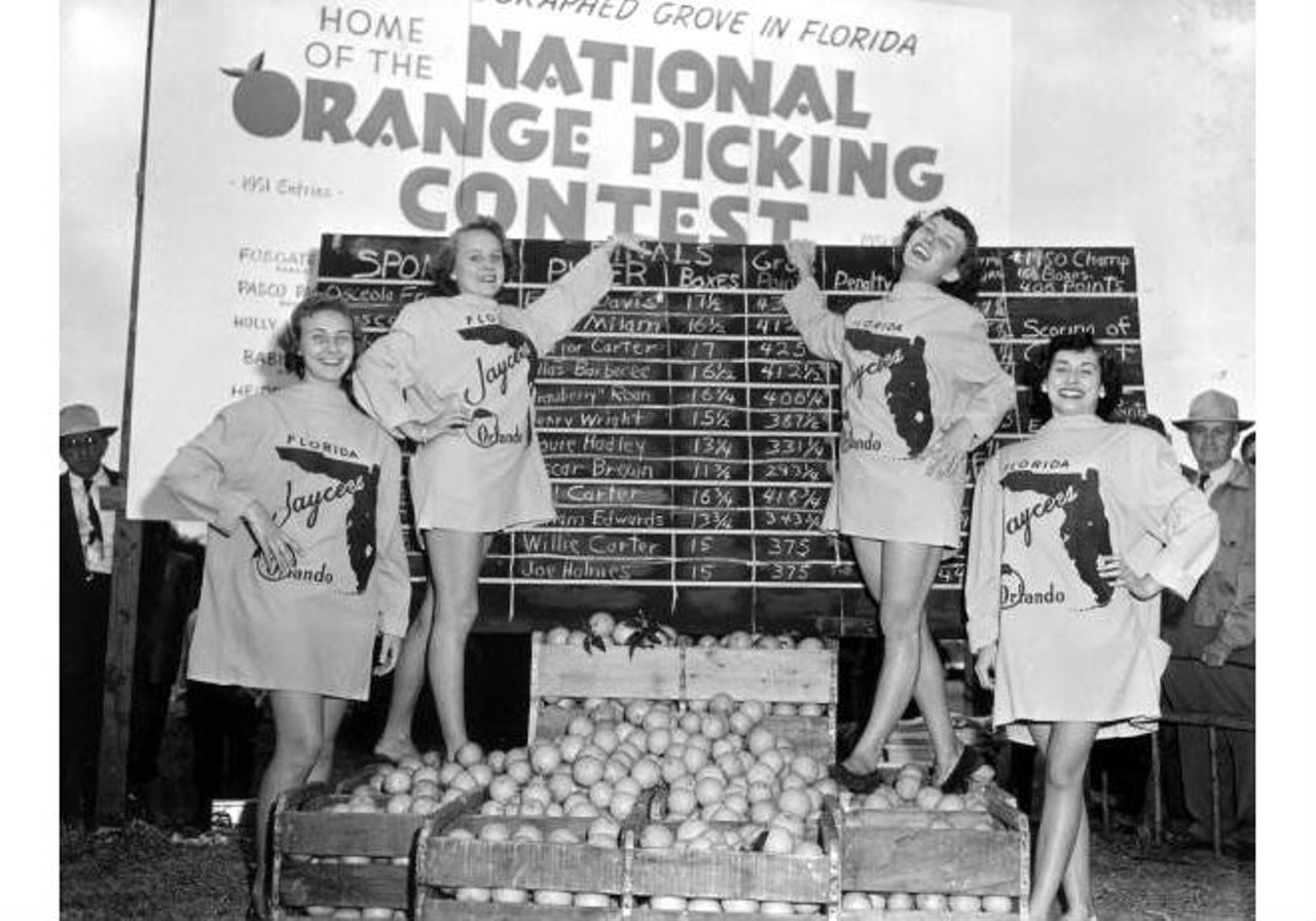 Young ladies pose with picked oranges in front of the scoreboard at contest
