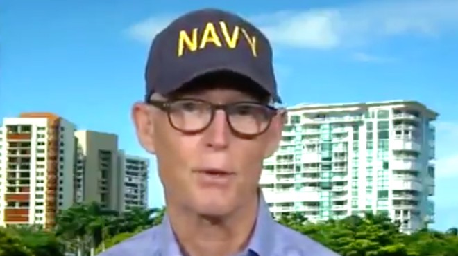 Sen. Rick Scott combines his Navy-hat schtick with his Woody Allen glasses.