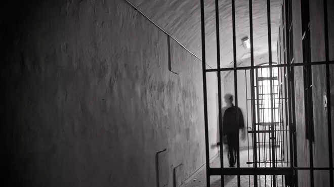 Black and white image of the inside of a prison with a man in shadow.