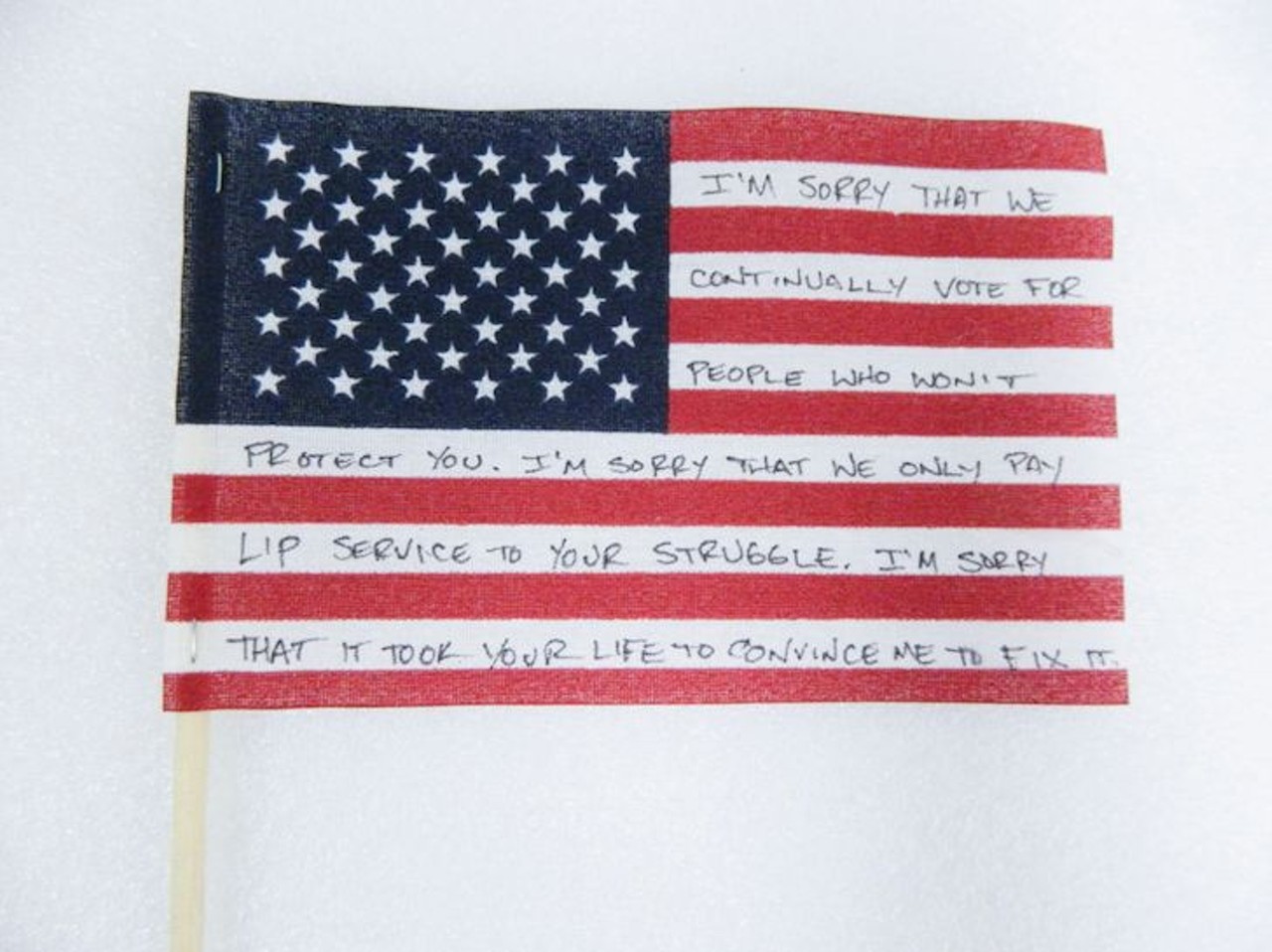 American Flag 
Description: 
Small American flag on a wooden stick with a message written on the white stripes in black that says, &#147;I&#146;M SORRY THAT WE CONTINUALLY VOTE FOR PEOPLE WHO WON&#146;T PROTECT YOU. I&#146;M SORRY THAT WE ONLY PAY LIP SERVICE TO YOUR STRUGGLE. I&#146;M SORRY THAT IT TOOK YOUR LIFE TO CONVINCE ME TO FIX IT.&#148;