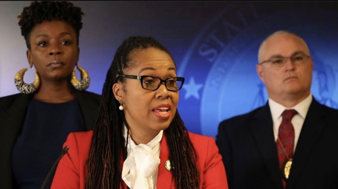Keisha Mulfort stands behind Monique Worrell at a press conference.