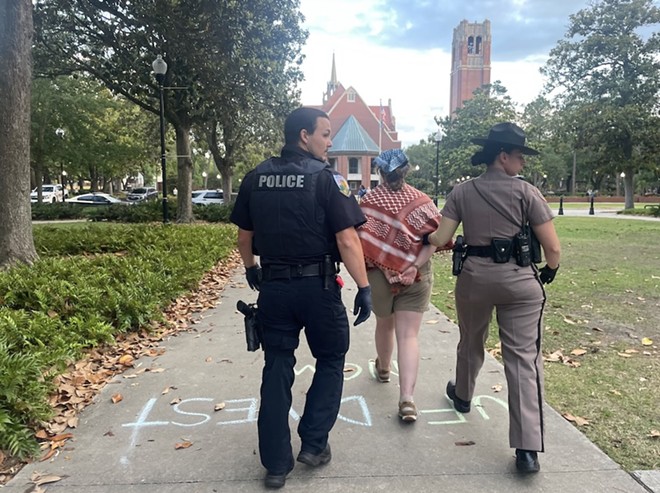 An unidentified University of Florida police officer and Florida Highway Patrol trooper walk a handcuffed protester away from the site on the university's campus where law enforcement arrested nine pro-Palestinian protesters late Monday, April 29, 2024. They were among the first such arrests on campuses in Florida. - Photo via Vivienne Serret/Fresh Take Florida
